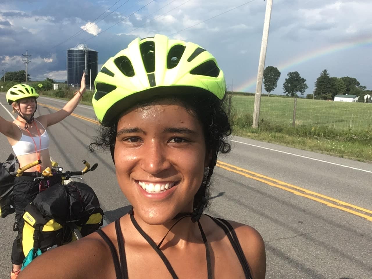 Picture of two females with sweaty foreheadswearing fluorescent yellow helmets on a cross country bike tour, smiling