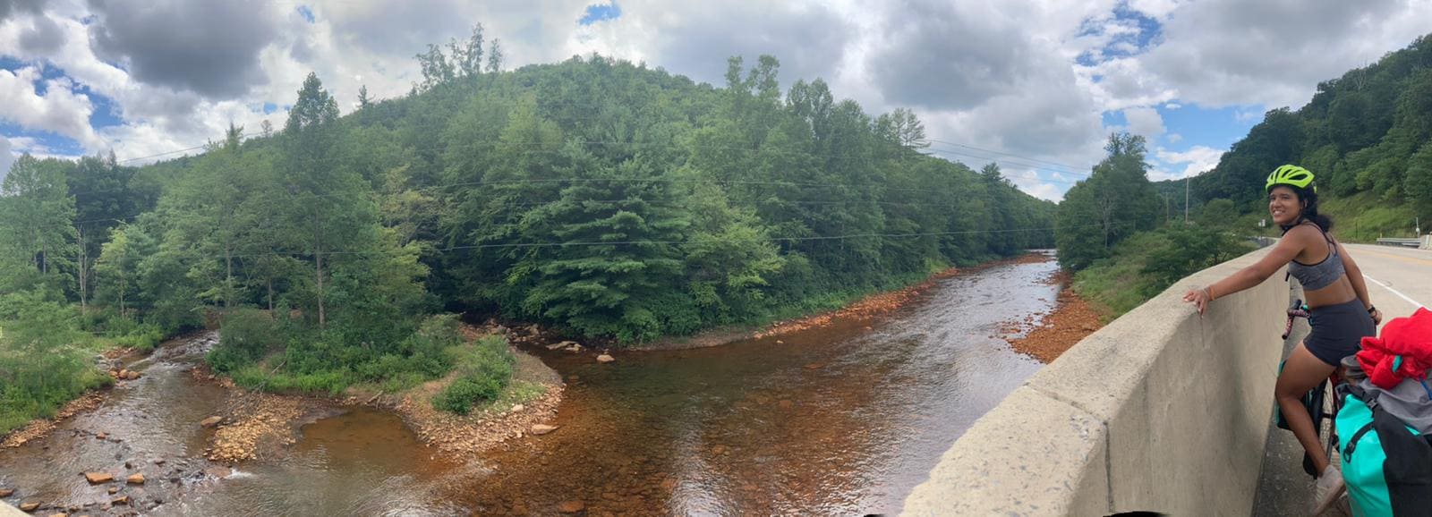 Panorama of a smiling girl on a bike overlooking a brown river