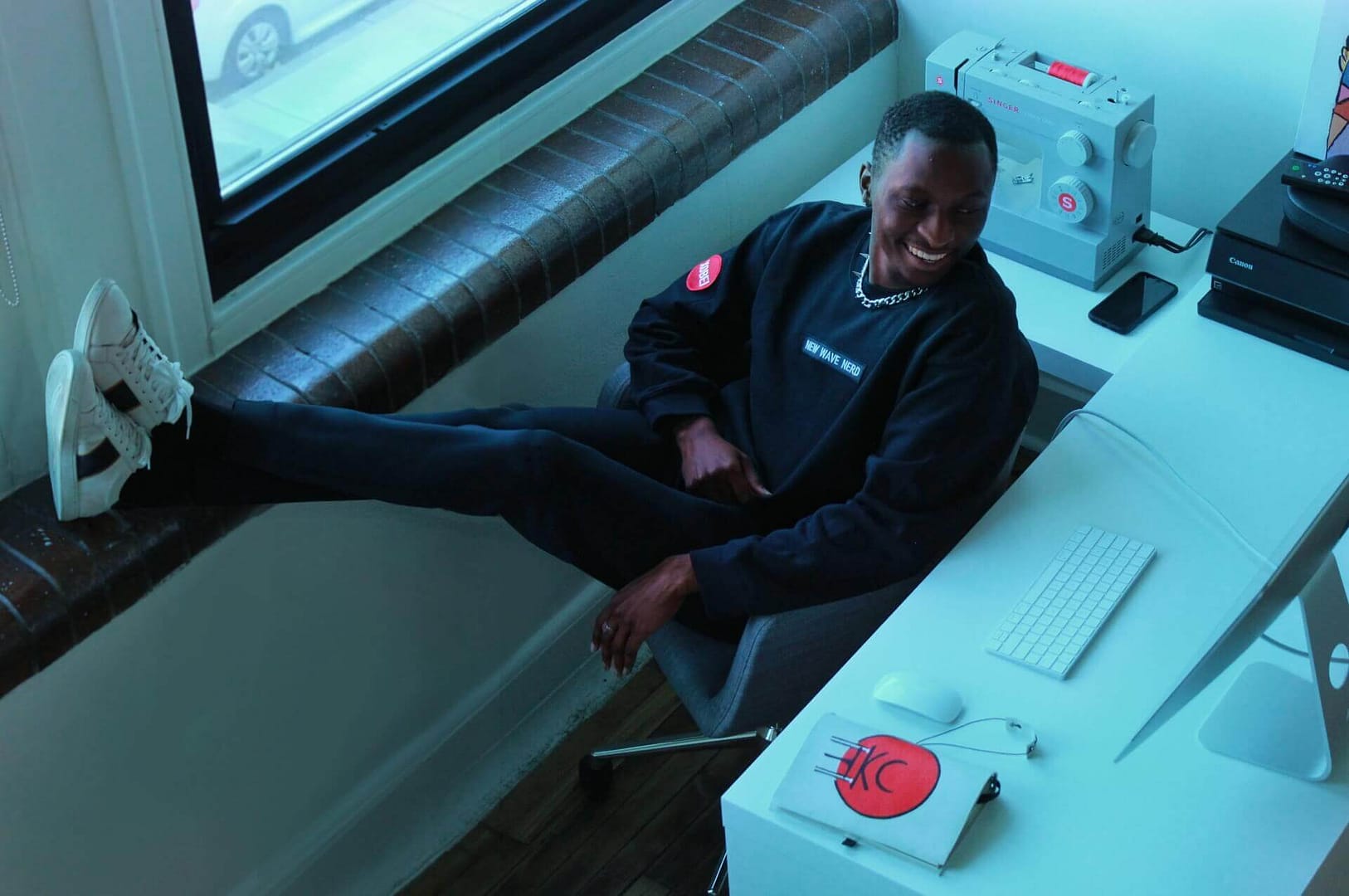 Cheikhou laughing with crossed legs on window sill modeling for Xobei